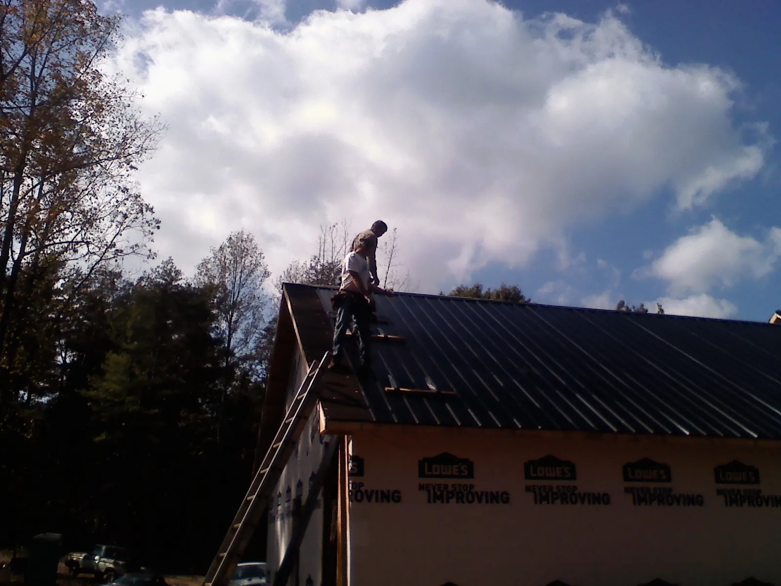 Roofer fastening dark metal panels high against a cloudy sky, from a Roof Inspection job in Satsop