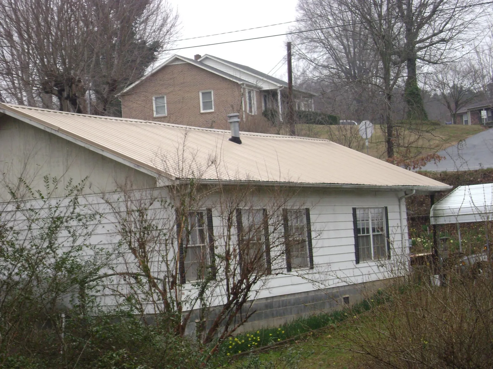 Tan metal roof on a white sided house set into a hillside — Commercial Roofing by Roofing Brothers in Satsop